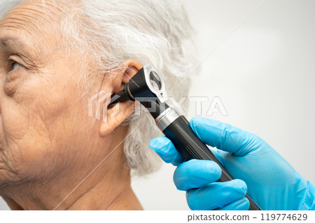 Otolaryngologist or ENT physician doctor examining senior patient ear with otoscope, hearing loss problem. 119774629