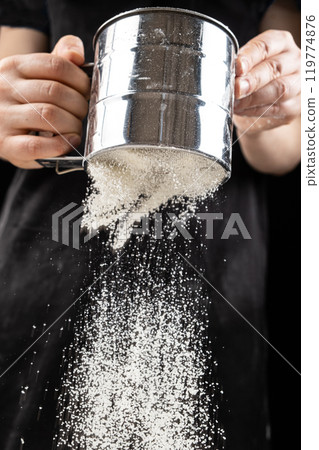 The cook sifts the wheat flour through a metal sieve 119774876