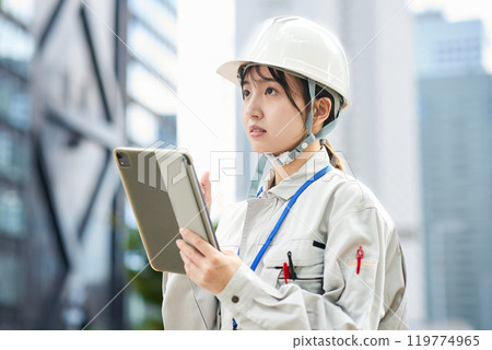 A young woman wearing work clothes and a helmet A young woman wearing work clothes and a helmet 119774965