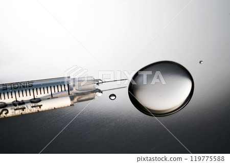 Injection syringe with a drop of drug on a stainless steel background. 119775588