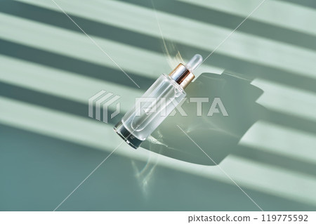 Bottle of cosmetic serum with pipette on green background with shadow stripes. Bottle of cosmetic serum with pipette on green background with shadow stripes. 119775592