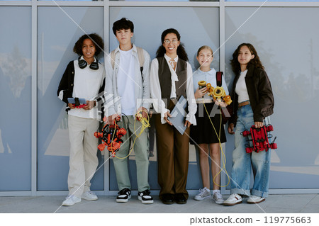Jolly multiracial secondary school students with multicolored robots standing next to smiling teacher with laptop while posing for portrait Jolly multiracial secondary school students with multicolored robots standing next to smiling teacher with laptop while posing for portrait 119775663