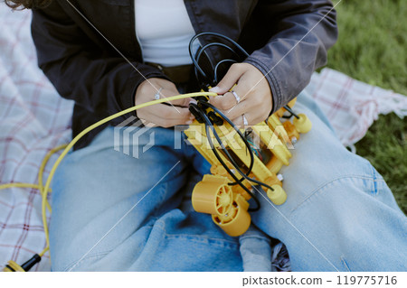 High angle shot of anonymous girl sitting on blanket and repairing yellow part of robot High angle shot of anonymous girl sitting on blanket and repairing yellow part of robot 119775716