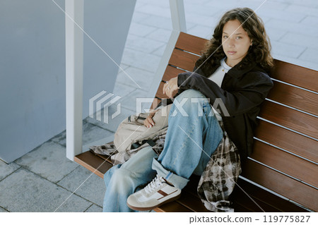 High angle portrait of teen girl resting on wooden bench in park 119775827