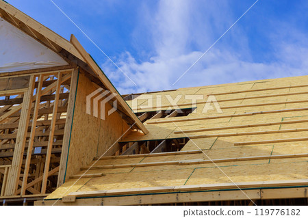 Plywood is installed on wooden roofing trusses at assembled roof of house in construction Plywood is installed on wooden roofing trusses at assembled roof of house in construction 119776182