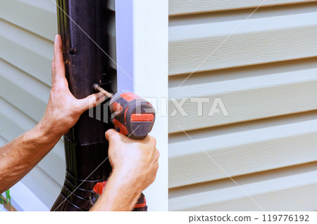 An employee installing rain gutter on roof with is installing downpipe, downspout bend 119776192