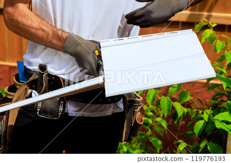 Workers cut plastic vinyl siding to size using scissors prior to installation 119776193