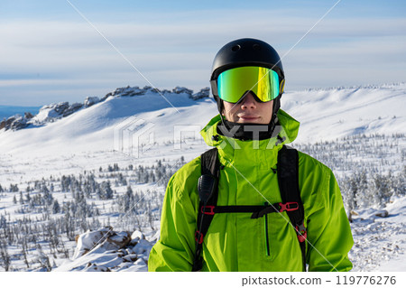 Close-up portrait of a skier or snowboarder in sports equipment, snowy mountains background at ski resort. 119776276