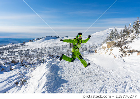 Man jumping Bright acid green outfit: warm suit, goggles, black helmet. snowy mountains background at ski resort. Man jumping Bright acid green outfit: warm suit, goggles, black helmet. snowy mountains background at ski resort. 119776277