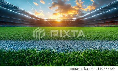 Close-up of a well-manicured football pitch under bright stadium lights, with a beautiful sunset in the background 119777822