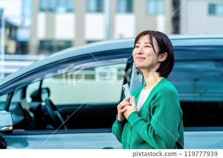 一名微笑的女士在汽車前拿著智慧型手機。 119777939