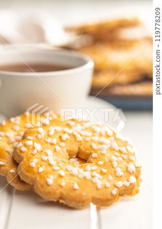 Sweet cookies in the shape of a flower. Tasty biscuits and cup of tea on white table. 119778209