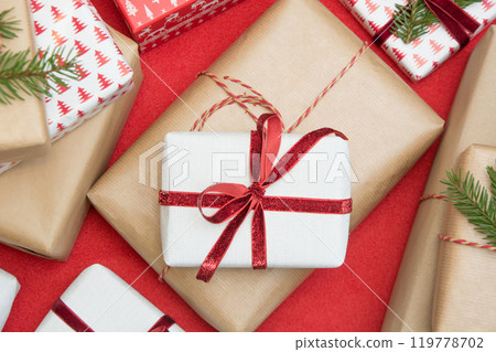 Christmas gift box wrapped in ornament paper and decorative red rope ribbon on red surface. Creative hobby, top view. Prepare to Xmas. Banner. 119778702