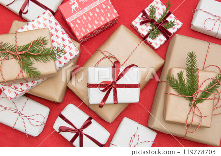 Christmas gift box wrapped in ornament paper and decorative red rope ribbon on red surface. Creative hobby, top view. Prepare to Xmas. Banner. 119778703