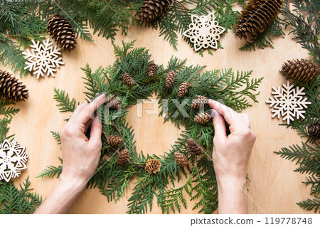 Preparation for Christmas holiday. Christmas composition of wreath, decor, dry orange, twigs and snowflakes. Woman prepare a wreath. Top view and copy space. Flat lay. Preparation for Christmas holiday. Christmas composition of wreath, decor, dry orange, twigs and snowflakes. Woman prepare a wreath. Top view and copy space. Flat lay. 119778748