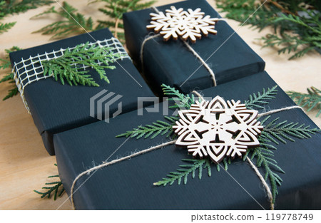 Christmas gift box wrapped in black paper with decor around branch cypress on wooden surface. 119778749