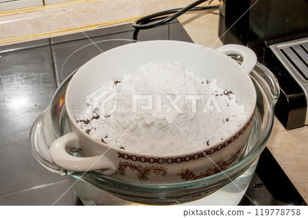 Powdered sugar, cocoa butter and grated cocoa in a container for making chocolate are heated in a water bath. 119778758