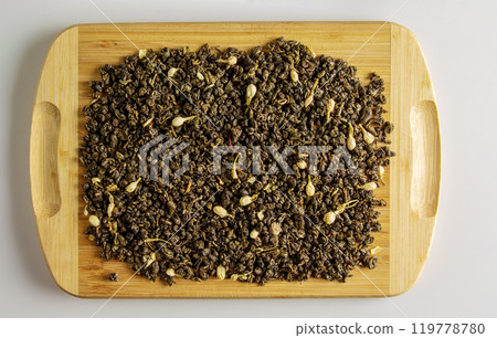 Green dry tea with jasmine flowers on a wooden board. Background and texture of dry tea. 119778780