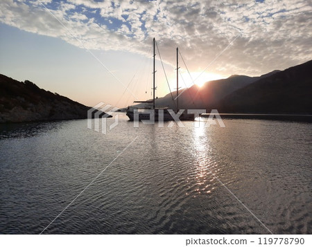 Yacht silhouette at sunset. A yacht in the sea against the backdrop of mountains, sky and clouds in sunset colors. 119778790