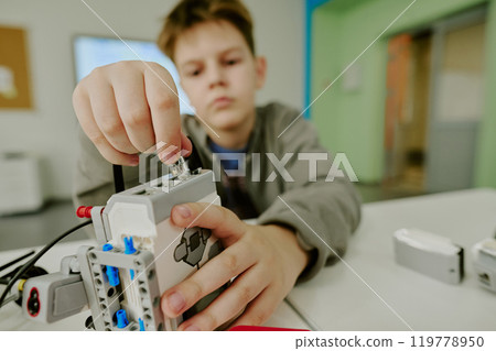 Medium close up of boys hand connecting wires to robot during robotics lesson 119778950
