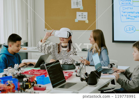 Teacher with smile looking at girl who enjoying VR game and trying to describe it while gesticulating in air Teacher with smile looking at girl who enjoying VR game and trying to describe it while gesticulating in air 119778991