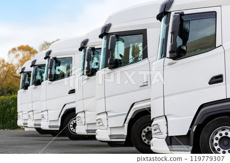 Fleet of new modern electric hybrid hydrogen or diesel white trucks parked in line row outdoors. Cargo freight industrial transportation logistics service. Commercial vehicles maintenance insurance Fleet of new modern electric hybrid hydrogen or diesel white trucks parked in line row outdoors. Cargo freight industrial transportation logistics service. Commercial vehicles maintenance insurance 119779307