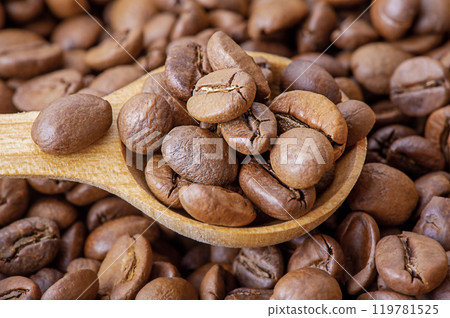 Roasted coffee beans in a wooden spoon on a coffee background. 119781525