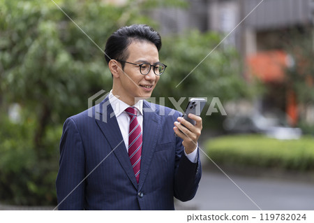 一位 40 歲左右的商人在城市裡看著他的智慧型手機螢幕 119782024