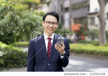 一位 30 多歲的商人戴著耳機，拿著智慧型手機，看著鏡頭 119782286