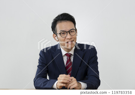 A businessman in his 40s wearing earphones and grimacing while looking at the camera A businessman in his 40s wearing earphones and grimacing while looking at the camera 119783358