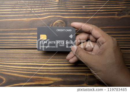 Human hand holding a debit or credit card with wooden background 119783485