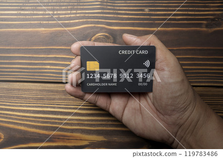 Human hand holding a debit or credit card with wooden background 119783486