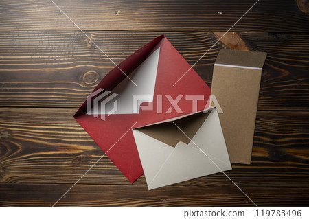 Top view of stack of three envelope and postcard on wooden background. The envelopes are of different variation size and colors 119783496