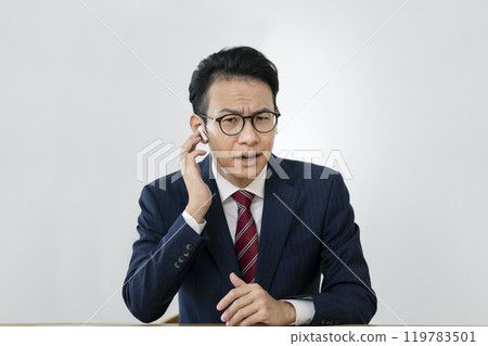 A businessman in his 40s wearing earphones and grimacing while looking at the camera 119783501