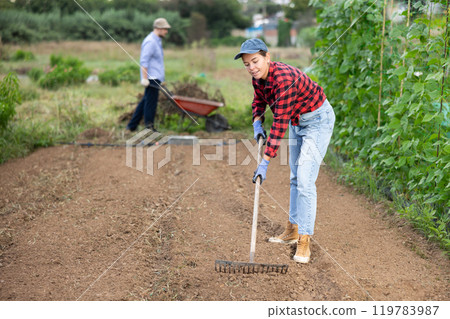 Girl working in garden, raking soil on patch while preparing for planting seedlings 119783987