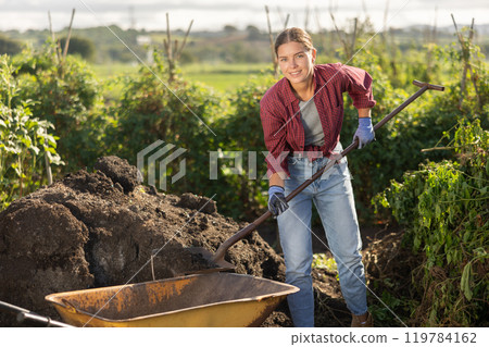 Woman puts black soil into a garden cart 119784162