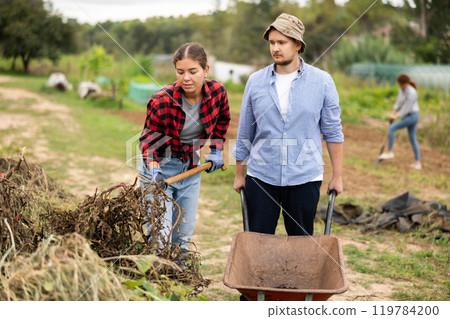 Woman and man takes out bunch of branches, puts garbage in wheelbarrow Woman and man takes out bunch of branches, puts garbage in wheelbarrow 119784200
