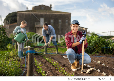 Woman with a garden tool near the beds in the garden Woman with a garden tool near the beds in the garden 119784295