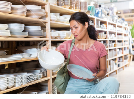 Positive female buyer chooses new plates in tableware store 119784353