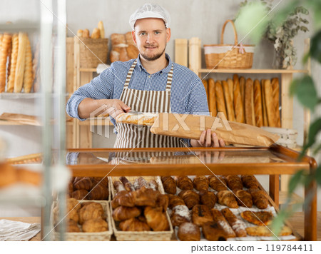 Bakery worker places fresh baguette in paper bag 119784411
