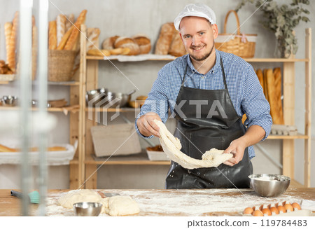 Professional baker prepares raw yeast dough in a bakery, shaping it into baguette 119784483