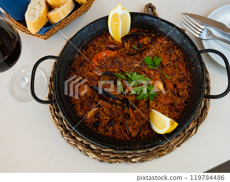 Traditional seafood paella with shrimps, squid and clams served in paellera Traditional seafood paella with shrimps, squid and clams served in paellera 119784486