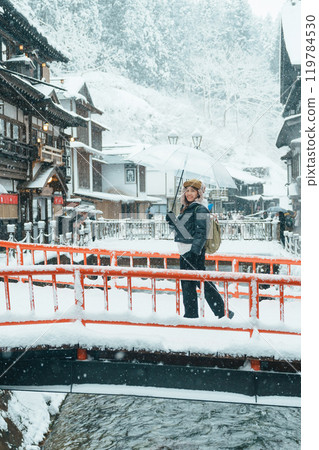 Woman tourist Visiting Ginzan Onsen in Yamagata, happy Traveler sightseeing Japanese Onsen village with Snow in winter season. landmark and popular for attraction in Japan. Travel and Vacation concept 119784530