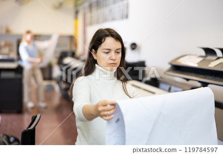 Printing establishment worker examining large piece of paper Printing establishment worker examining large piece of paper 119784597
