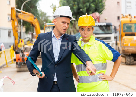 Civil engineer discussing a construction plan with a young woman worker shows her something 119784649