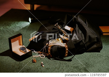 Huge black bag full of golden accessories and jewelry on deep green carpet Huge black bag full of golden accessories and jewelry on deep green carpet 119785597