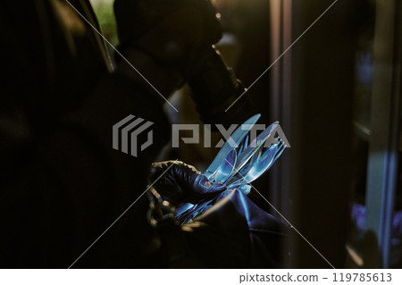 Medium close up of unrecognizable thies hands in black leather gloves holding silverware under flashlight 119785613