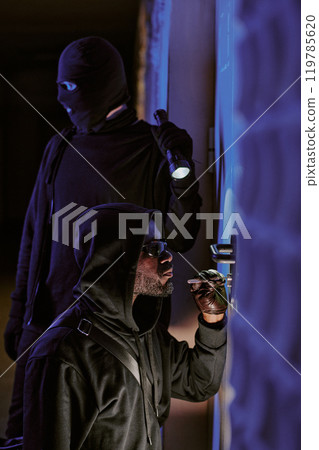Vertical shot of two crime partners picking lock together at late night trying to enter house Vertical shot of two crime partners picking lock together at late night trying to enter house 119785620