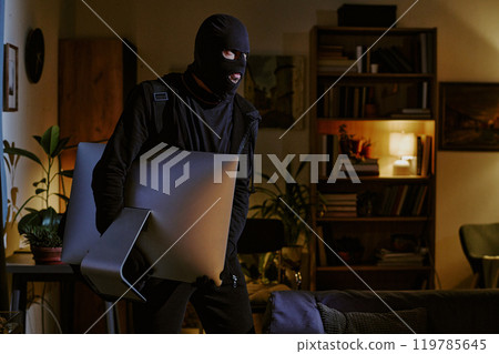 Thieve in black clothes and balaclava grabbing huge monitor in dimly lit room Thieve in black clothes and balaclava grabbing huge monitor in dimly lit room 119785645