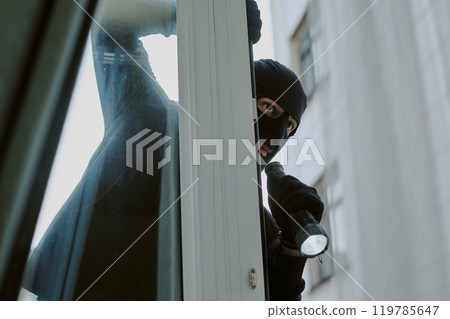 Low angle shot of unrecognizable thief in balaclava with flashlight seeing apartment from window Low angle shot of unrecognizable thief in balaclava with flashlight seeing apartment from window 119785647